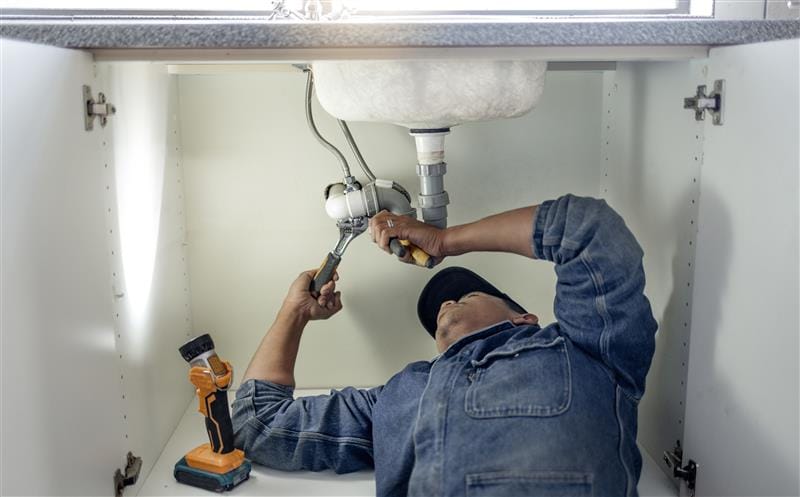 Plumber repairing pipes beneath a bathroom sink in Apollo Beach