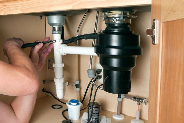 Plumber installing a garbage disposal beneath a kitchen sink in Apollo Beach