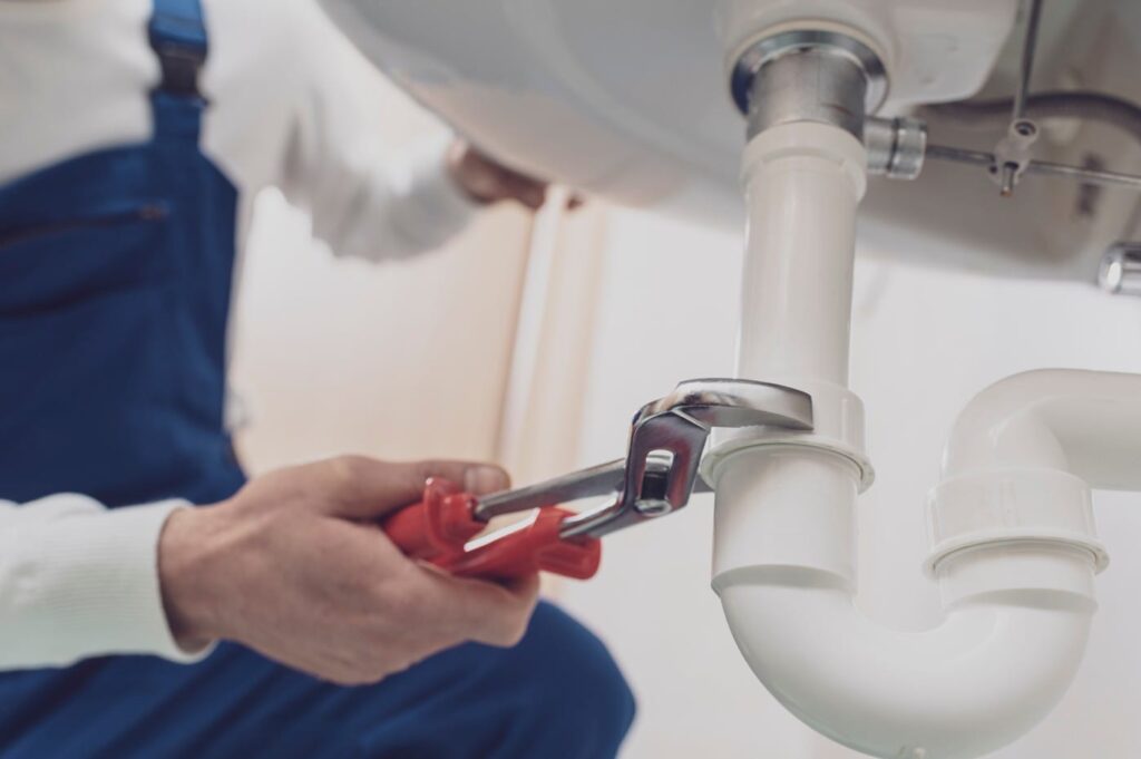 Plumber repairing a white drain pipe beneath a sink in Apollo Beach